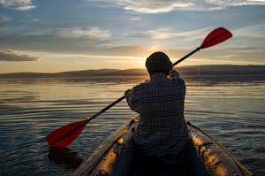 Person kayaking at sunset with plaid shirt and beanie on calm water